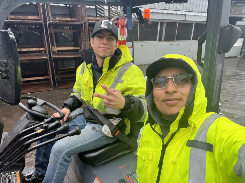 Chel and a coworker on a forklift in hi vis jackets